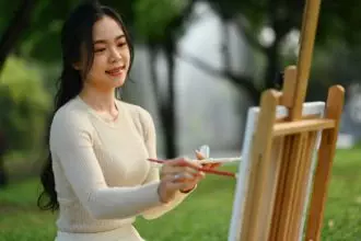 Smiling young woman painting a picture in the park. Art therapy and creative hobbies concept